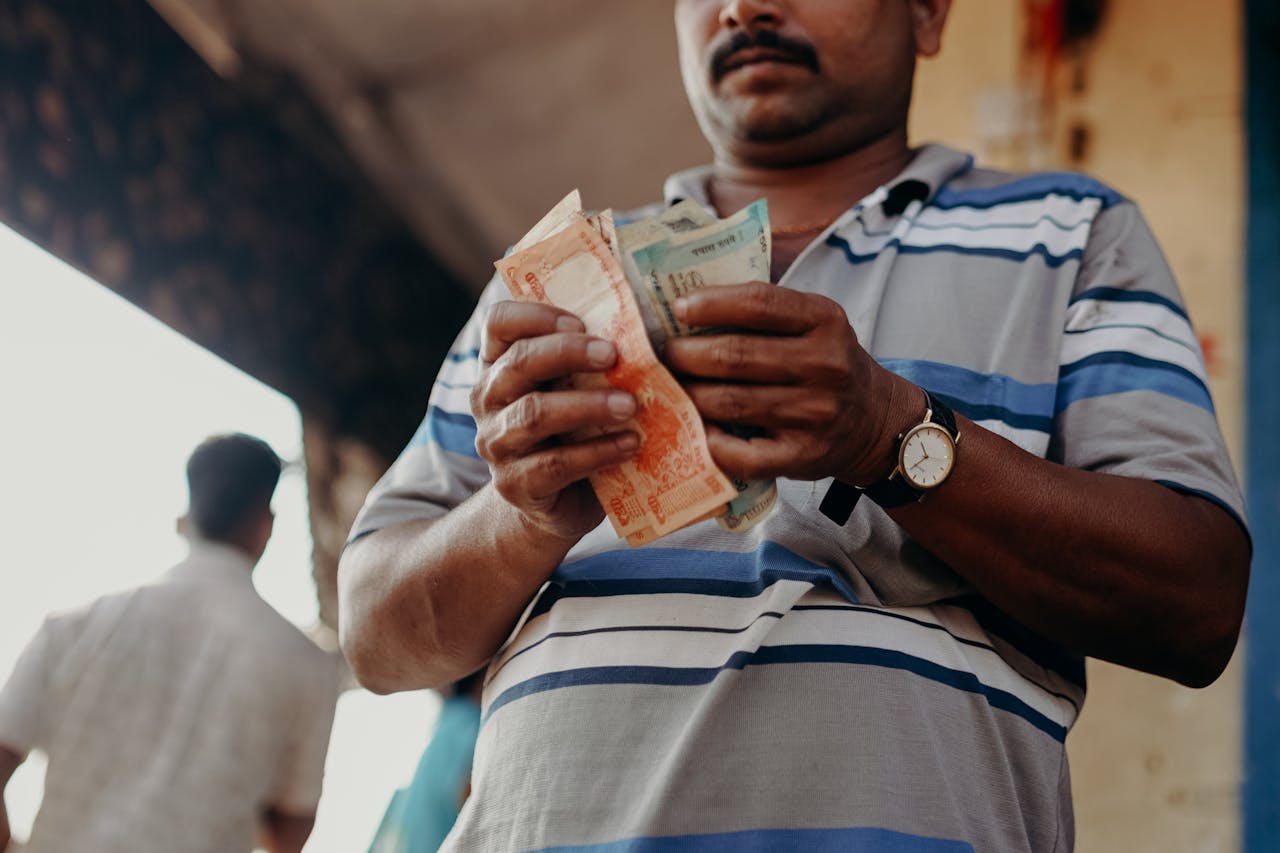 Man in Indian market counting rupee notes, showcasing daily street commerce.